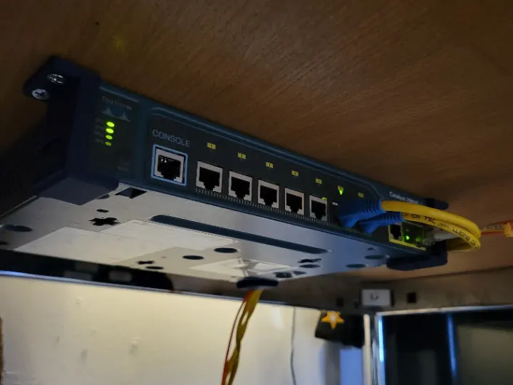 3D printed screw in brackets mounting a Cisco 2960 switch to the underside of a desk.