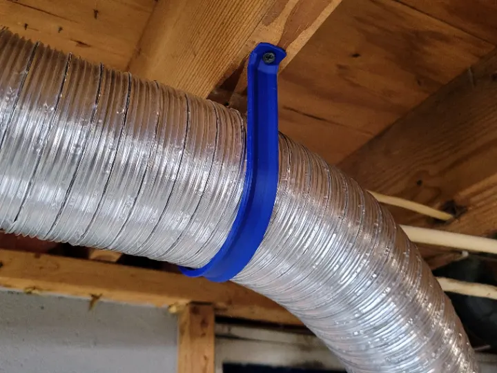 A 3D printed bracket holding up ventilation duct in an unfinished basement.